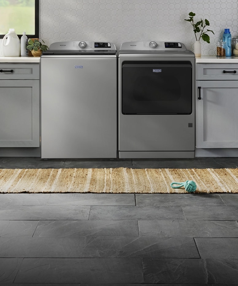 A top load laundry pair in a laundry room with pet toys laying around.