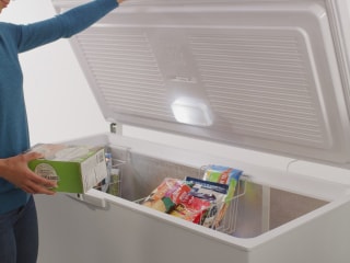 A person placing an item into an open Maytag® chest freezer