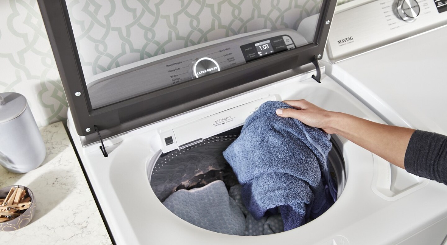 Hand loading a top load washer with towels and blankets