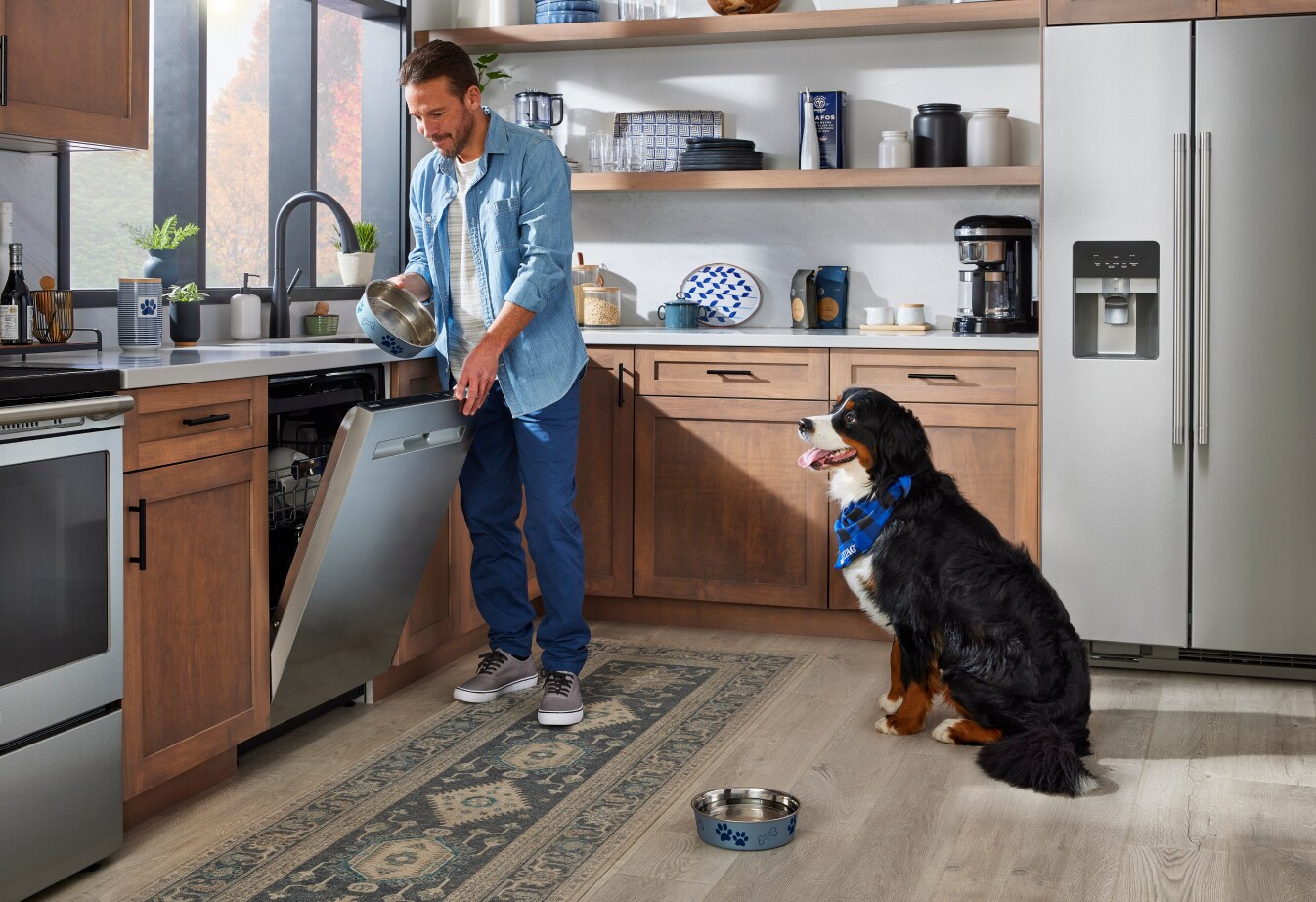A person loading their Maytag® dishwasher with a dog in the kitchen
