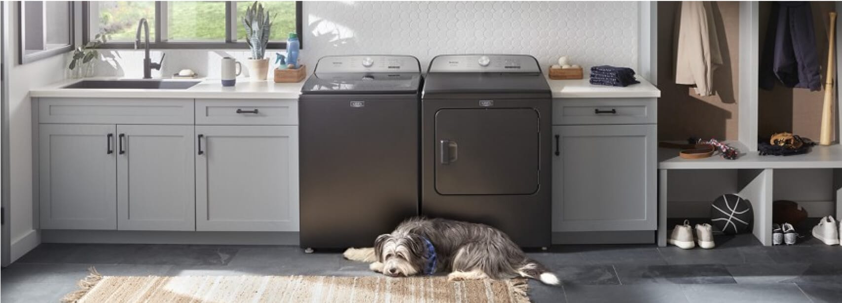 A Maytag® washer and dryer in a laundry room with white cabinets and dog laying on the floor