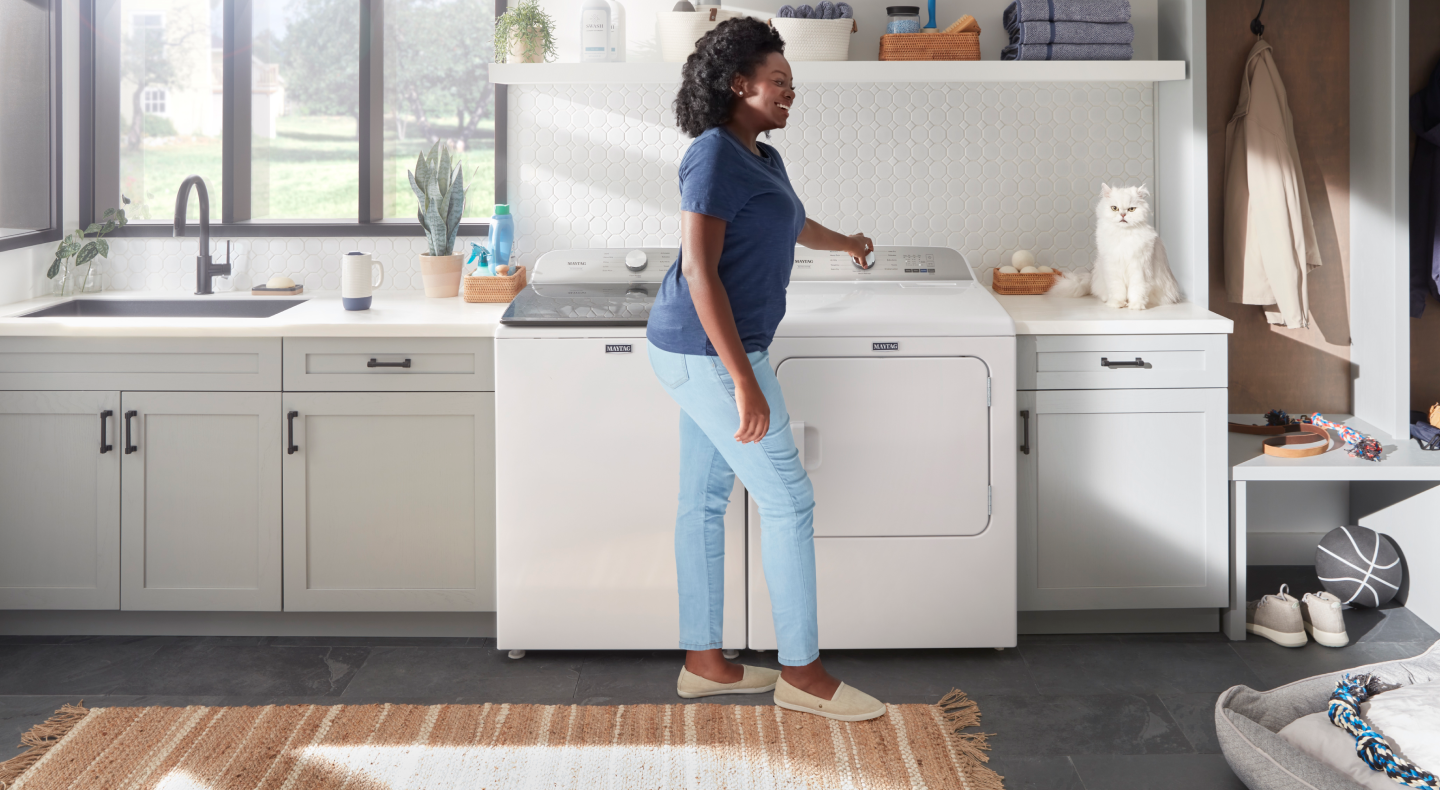 Person standing in front of a white Maytag® top load washer and dryer set Person standing in front of a white Maytag® top load washer and dryer set