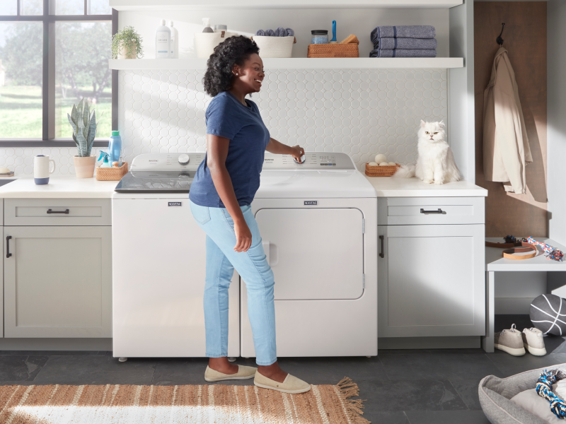 Person standing in front of a white Maytag® top load washer and dryer set Person standing in front of a white Maytag® top load washer and dryer set