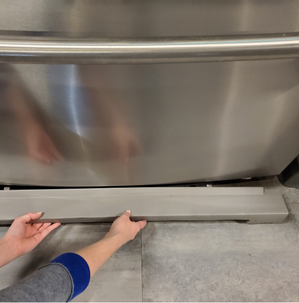 Hands replacing the base grille on a refrigerator.
