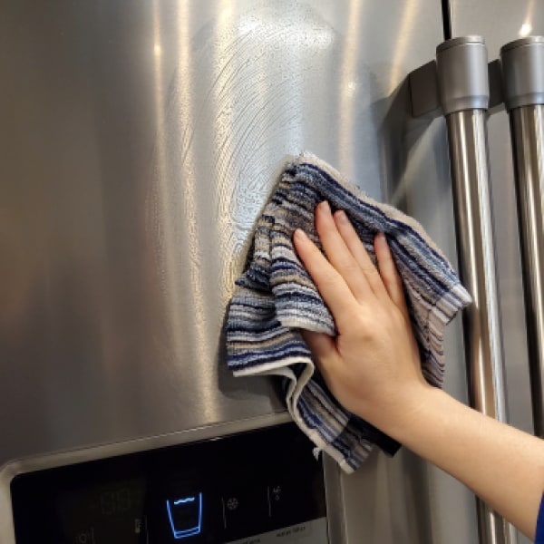 A hand rinsing the outside of a refrigerator door with a cloth.