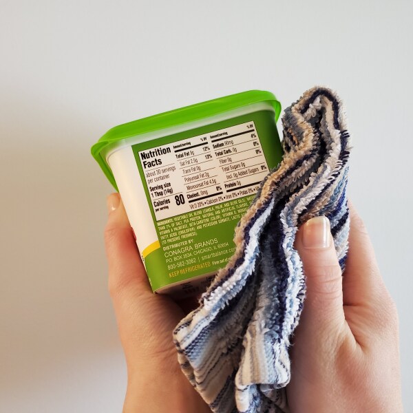 A container of butter being wiped down with a cloth.