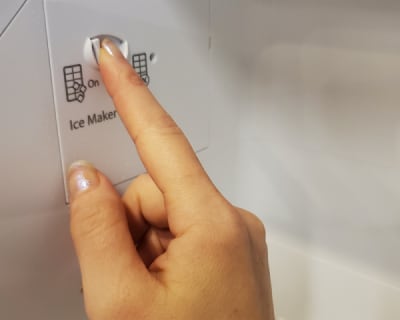 A finger pressing an ice maker button