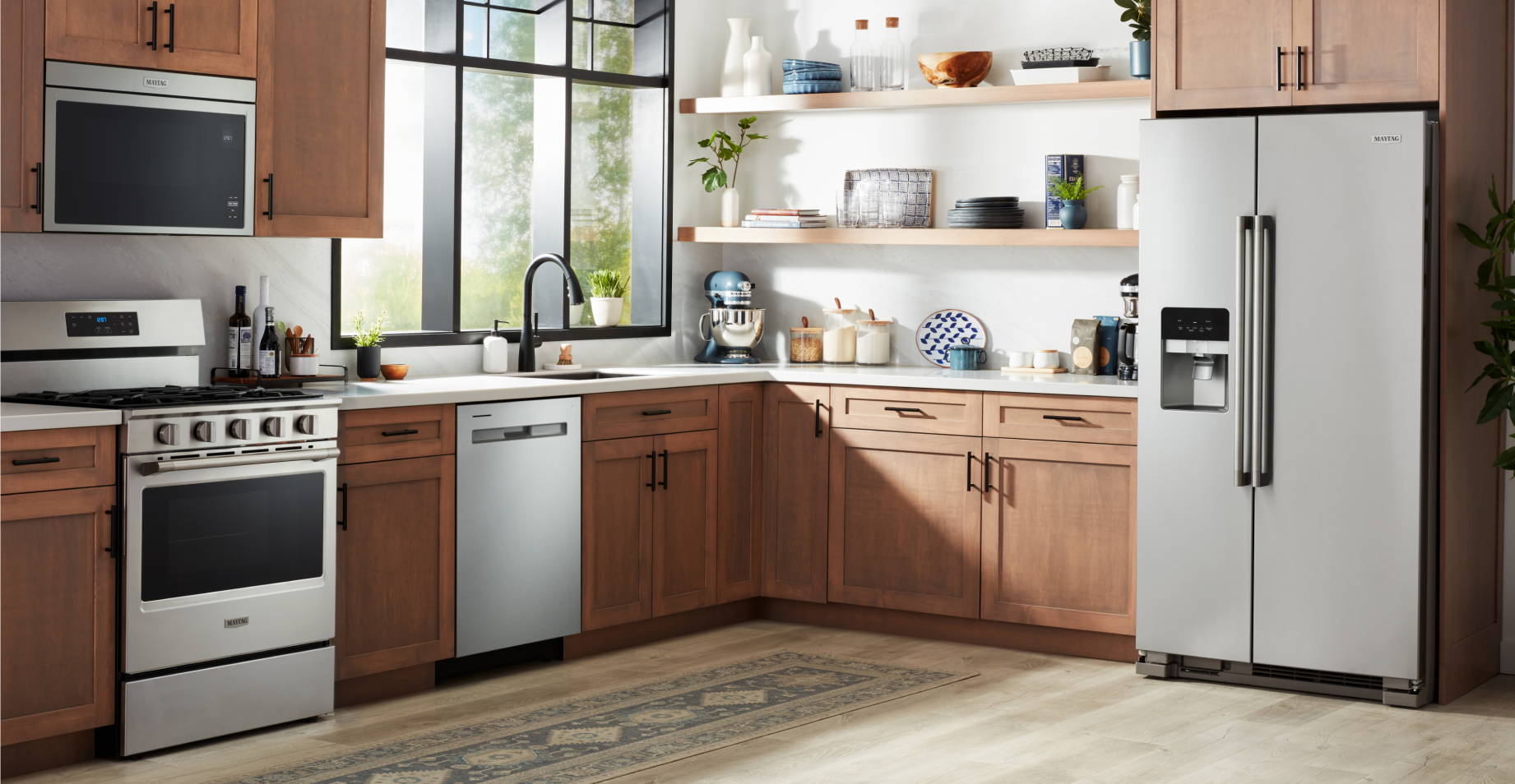 The Maytag® Performance Lineup refrigerator, over-the-range microwave, freestanding electric range and dishwasher in a kitchen with light brown cabinets