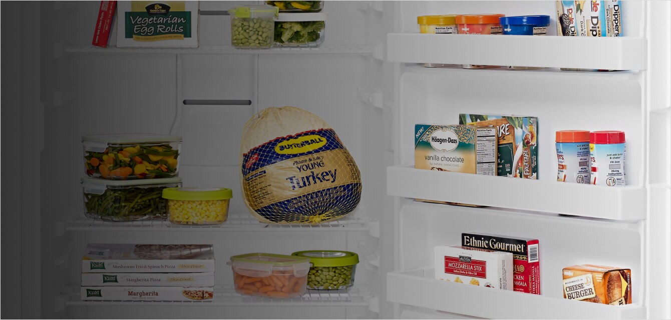 A frozen turkey and other frozen food inside a Maytag® upright freezer.