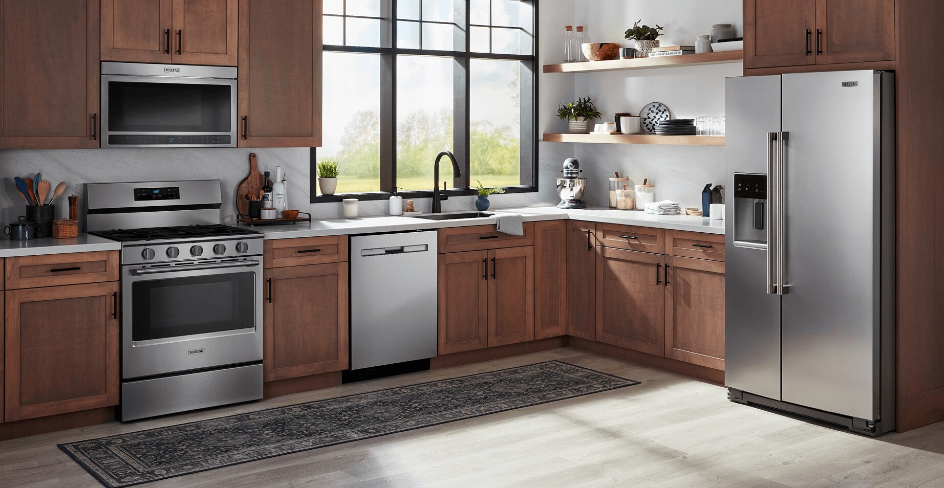 The Maytag® Performance Lineup refrigerator, over-the-range microwave, freestanding electric range and dishwasher in a kitchen with light brown cabinets