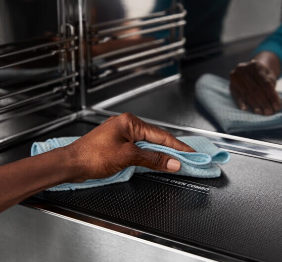 A hand holding a towel, cleaning the bottom of a microwave oven.