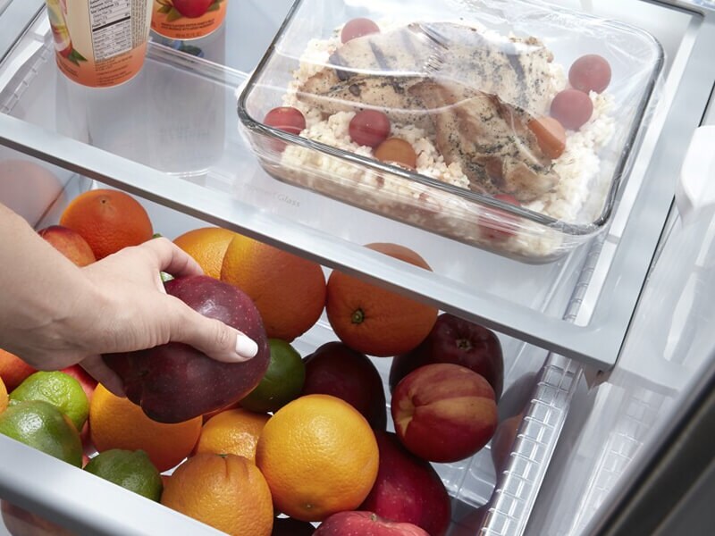 Person placing an apple inside a refrigerator drawer