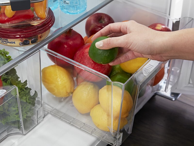Person placing a lime inside a refrigerator drawer