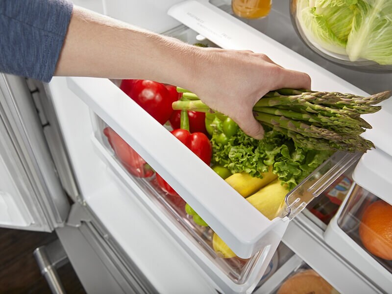 Person placing a bundle of asparagus inside a refrigerator drawer