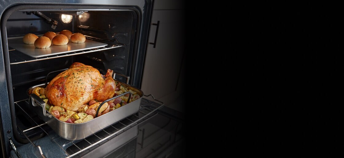 Whole chicken and rolls inside an oven