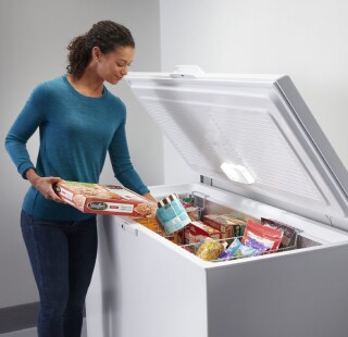 Person loading frozen food into a chest freezer