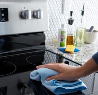 A hand cleaning a glass cooktop with a blue rag