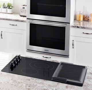 An induction cooktop with a double wall oven in the background