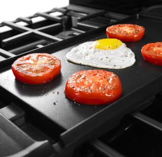 An egg and four tomatoes on a griddle