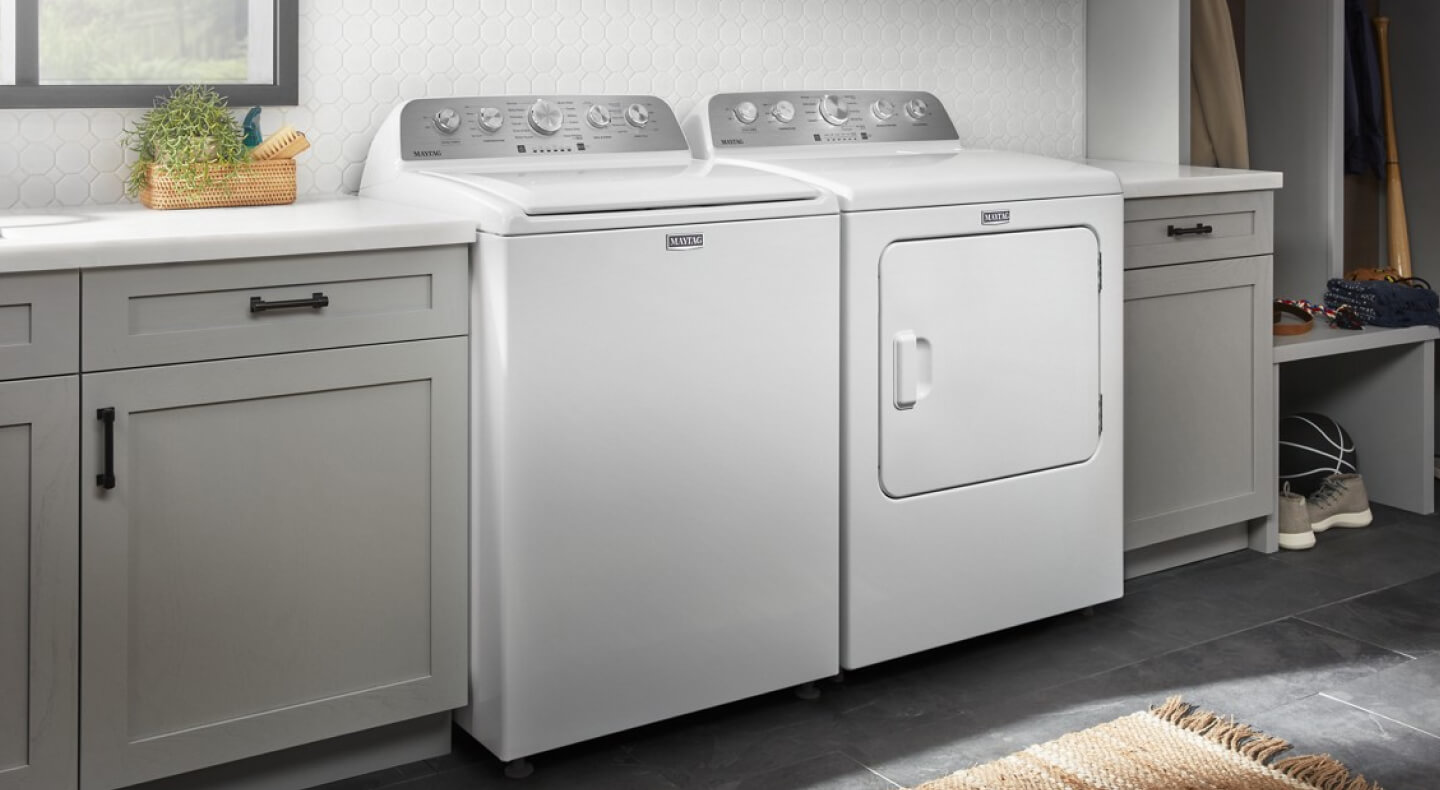 A white Maytag® top load washer and dryer next to grey cabinetry