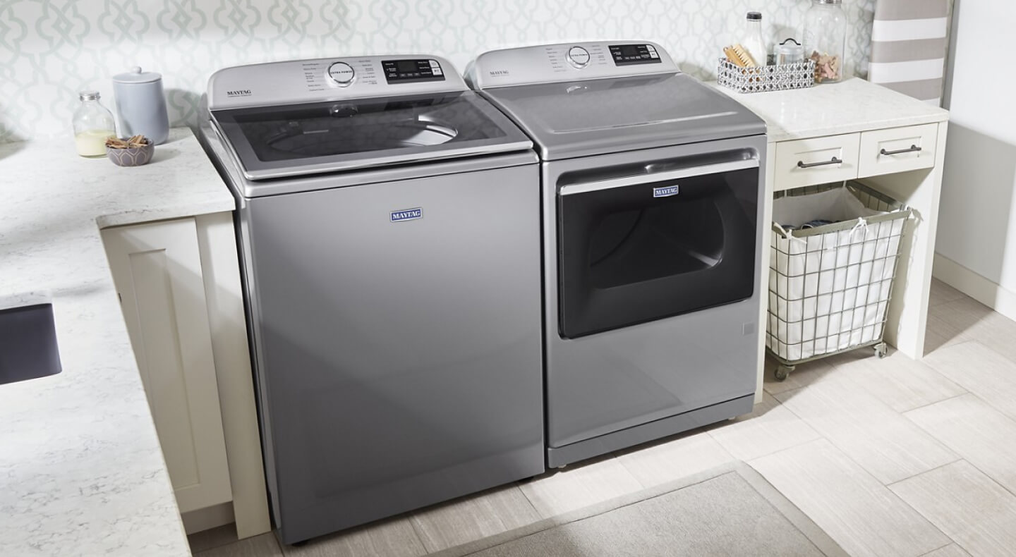 Maytag® top load washer and dryer in between cream cabinetry in a laundry room