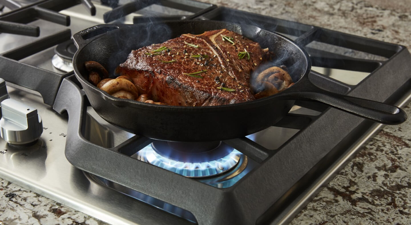 A close-up of food searing on a Maytag® gas cooktop