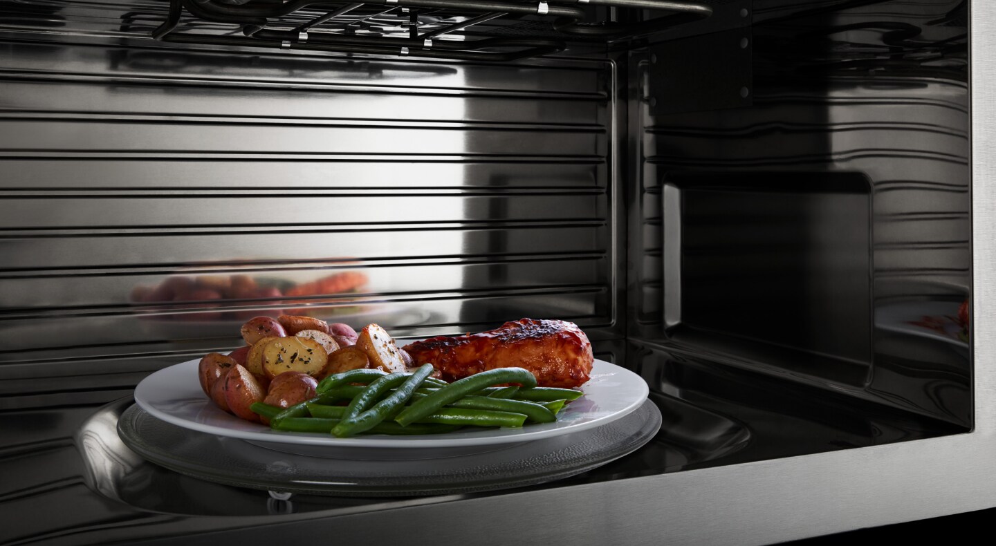 A closeup of the interior of a convection Maytag® microwave heating chicken, potatoes and beans A closeup of the interior of a convection Maytag® microwave heating chicken, potatoes and beans