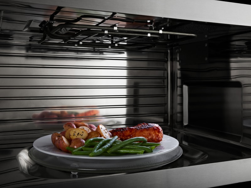 A closeup of the interior of a convection Maytag® microwave heating chicken, potatoes and beans A closeup of the interior of a convection Maytag® microwave heating chicken, potatoes and beans