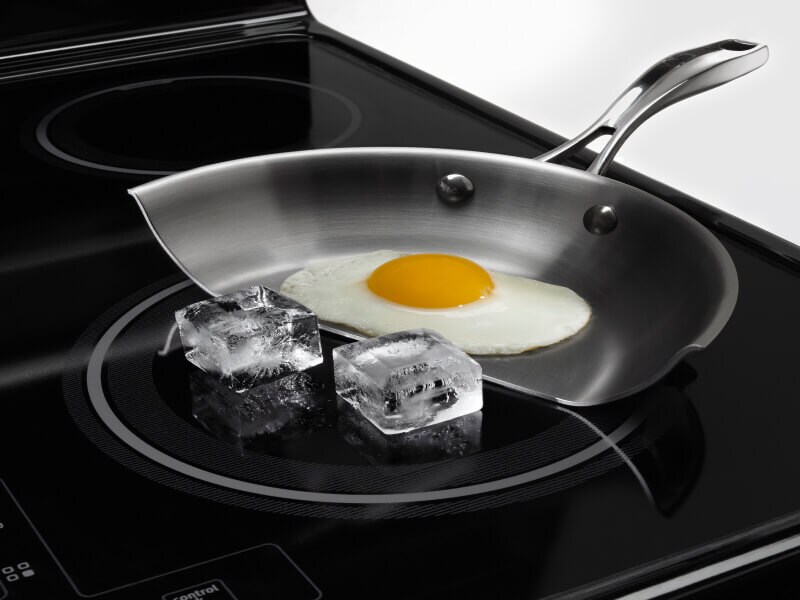 Egg cooking in a partial frying pan next to ice on a cooktop