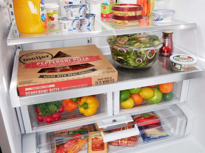 Open refrigerator with a view of full drawers with citrus and vegetables inside