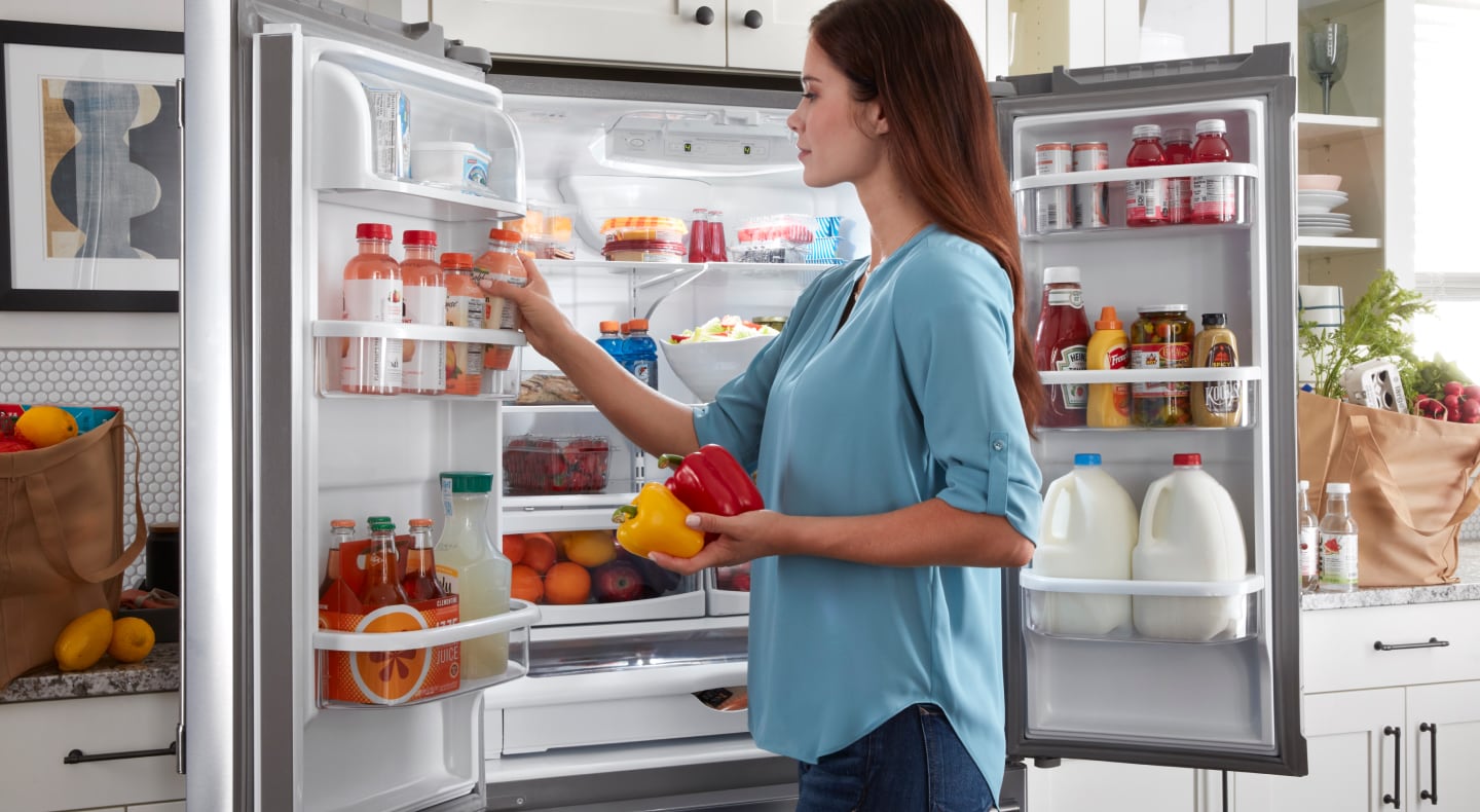 Person standing at an open fridge putting produce away Person standing at an open fridge putting produce away