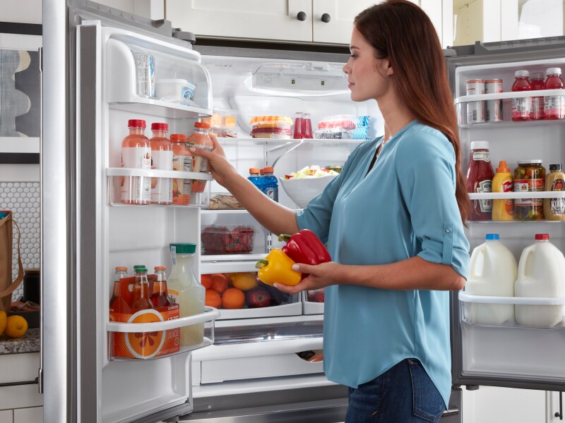 Person standing at an open fridge putting produce away Person standing at an open fridge putting produce away