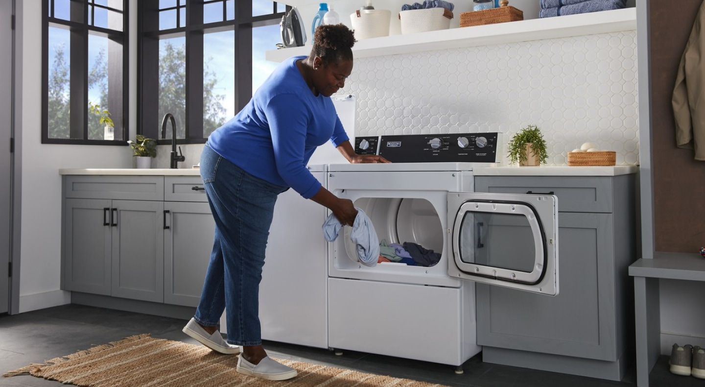 Person loading clothes into a commercial-grade dryer Person loading clothes into a commercial-grade dryer