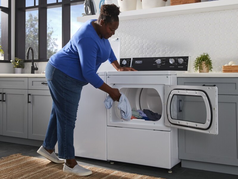 Person loading clothes into a commercial-grade dryer Person loading clothes into a commercial-grade dryer