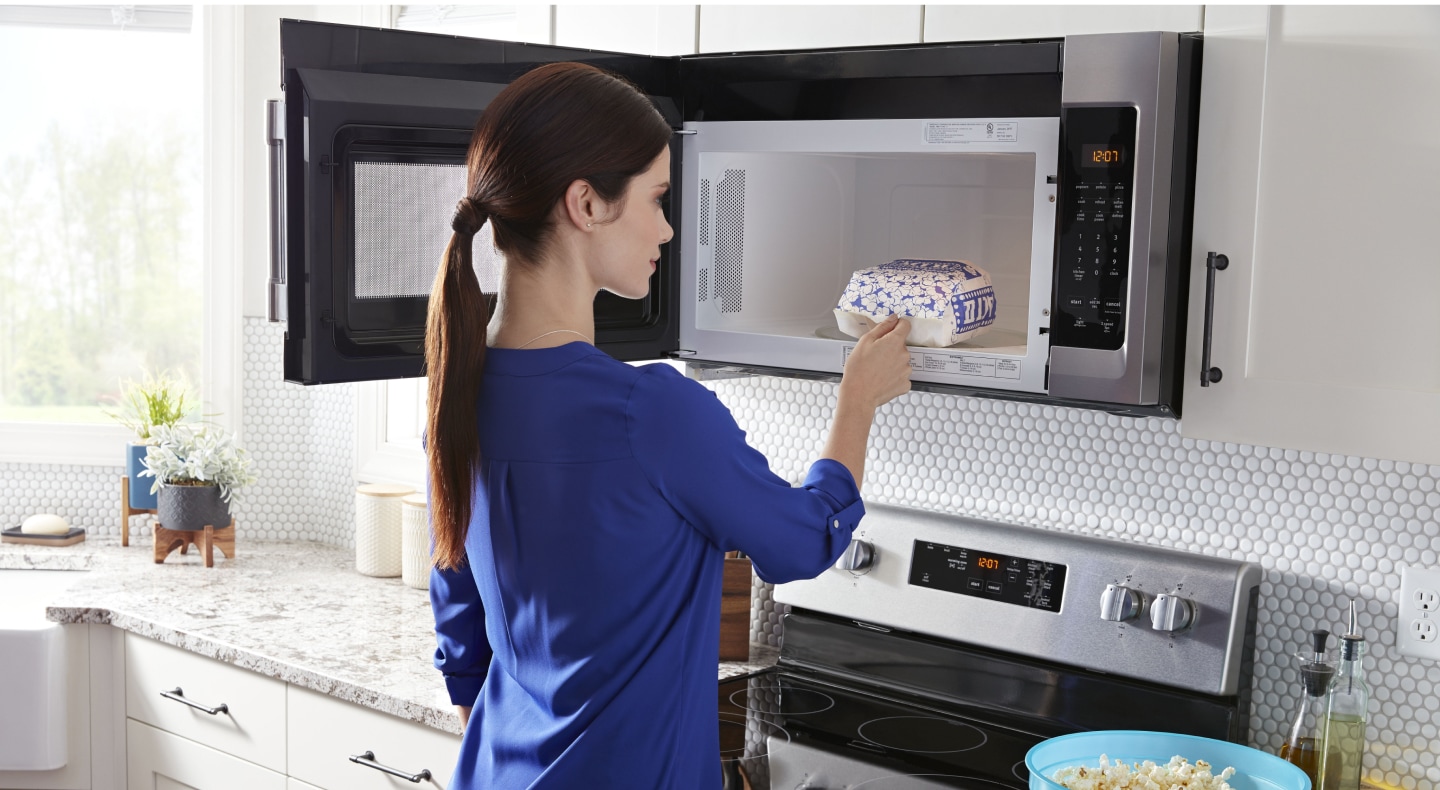 Person removing popcorn from an over-the-range microwave Person removing popcorn from an over-the-range microwave
