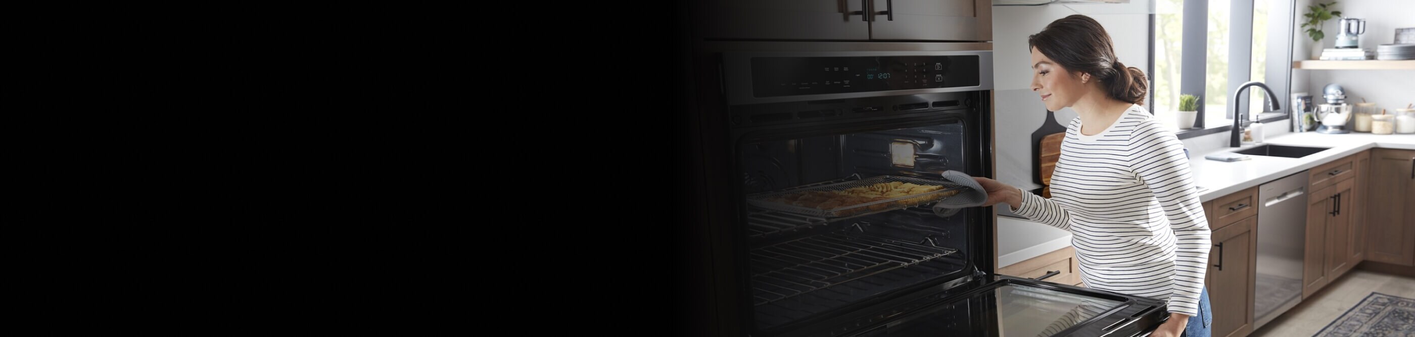 Person removing a baking tray from a Maytag® wall oven
