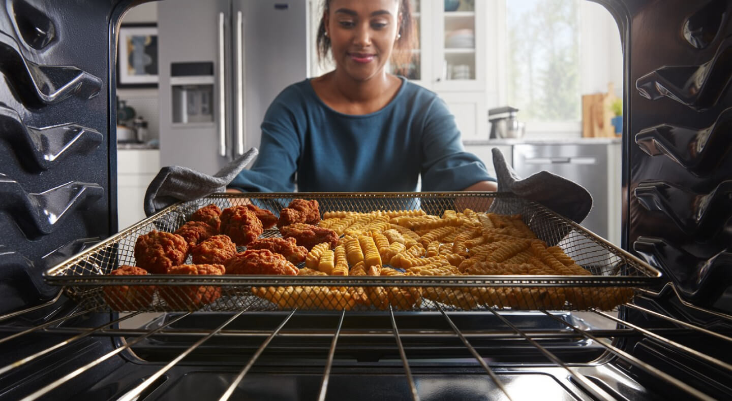 Person removing chicken strips and fries from an oven