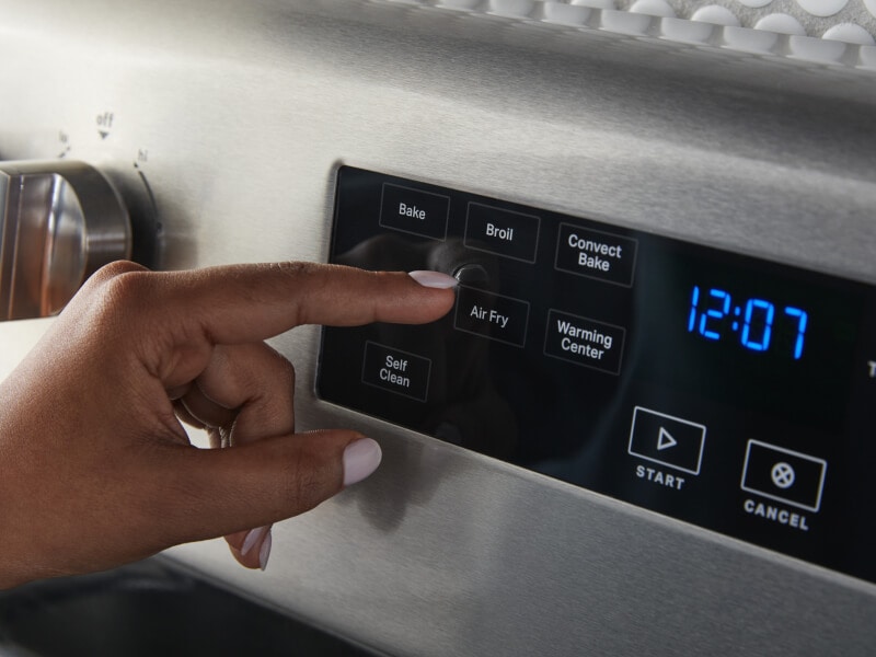 Finger pressing the Air Fry button on a stainless steel oven Finger pressing the Air Fry button on a stainless steel oven