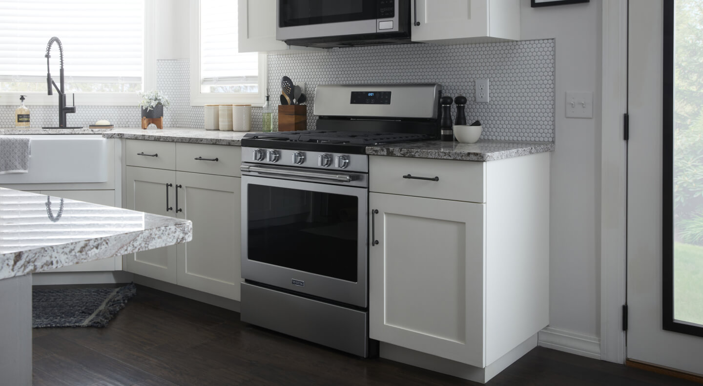Stainless steel Maytag® gas range surrounded by white cabinets