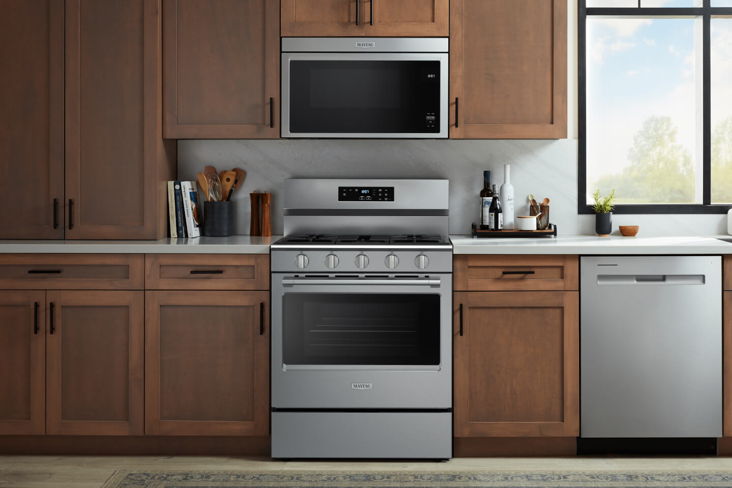Stainless appliances in a kitchen with medium wood cabinets with black hardware