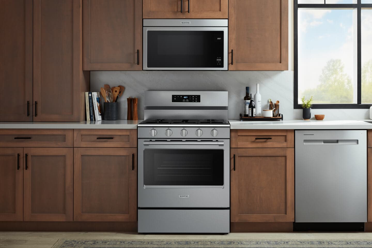 Stainless appliances in a kitchen with medium wood cabinets with black hardware