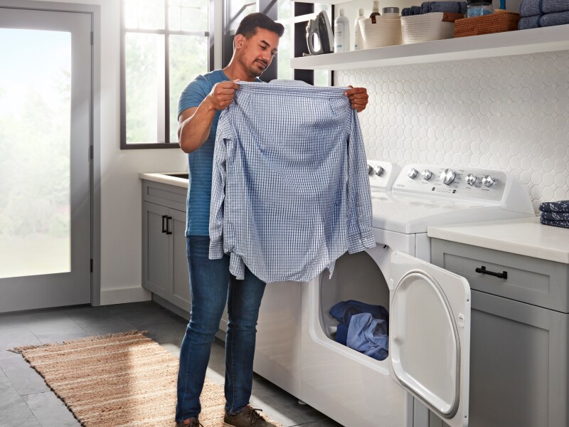 Person removes blue shirt from a Maytag® dryer in laundry room