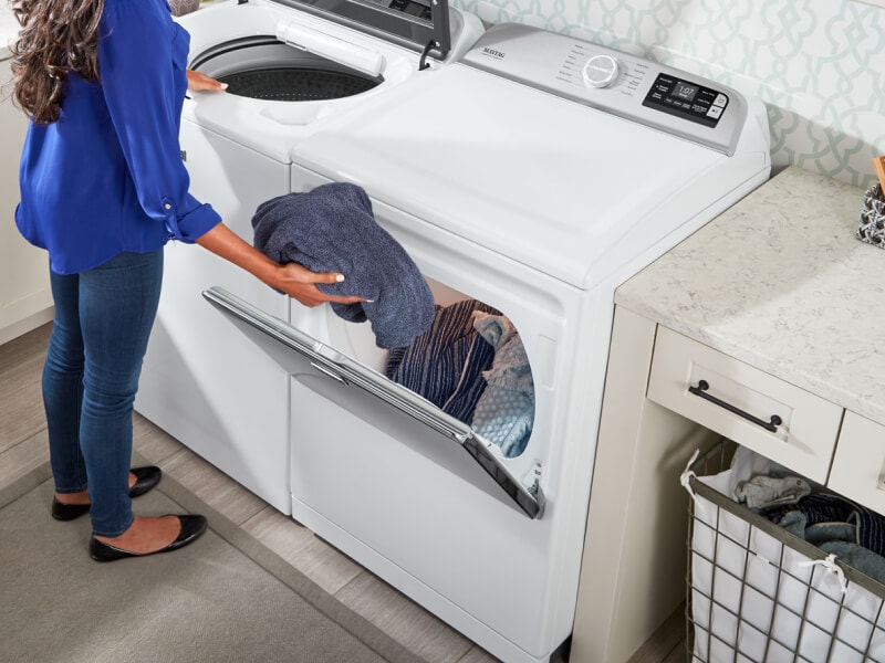 A woman placing a towel into a large capacity dryer