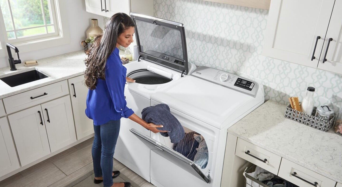 A woman loading washed laundry into a dryer A woman loading washed laundry into a dryer