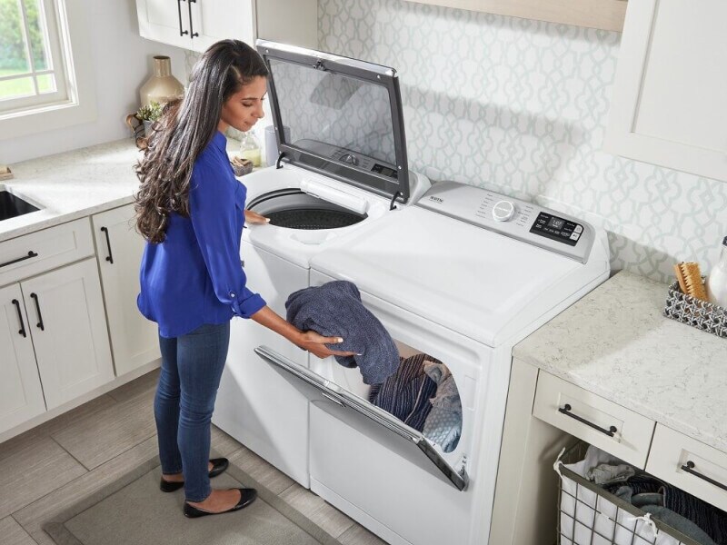 A woman loading washed laundry into a dryer A woman loading washed laundry into a dryer
