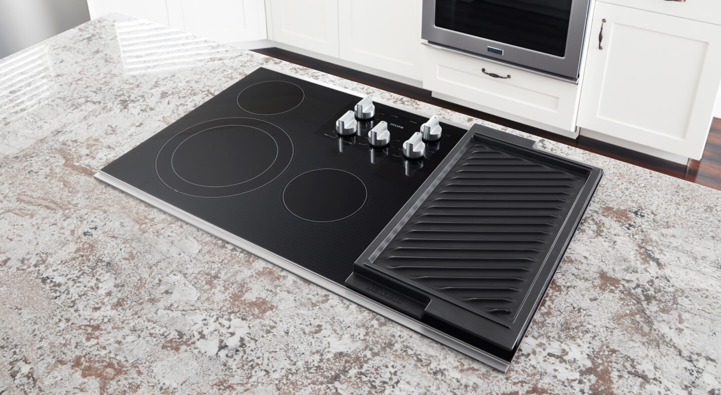 An electric cooktop with griddle installed in the granite counter of a kitchen island