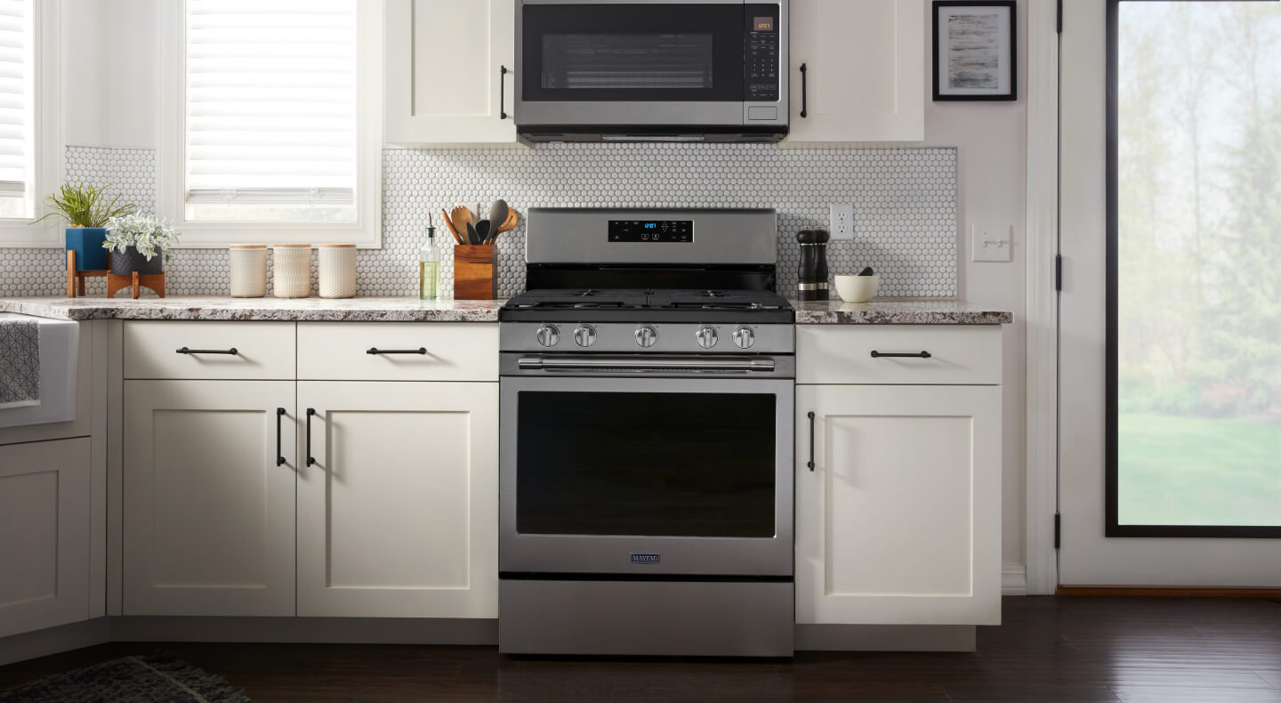 Maytag® stainless steel range between white cabinetry beneath over-the-range microwave Maytag® stainless steel range between white cabinetry beneath over-the-range microwave