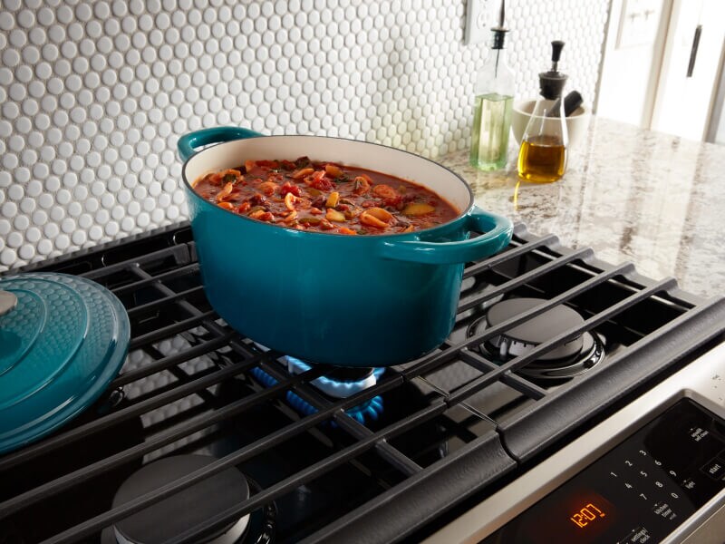 Blue, oval dutch oven on grates above gas burner Blue, oval dutch oven on grates above gas burner