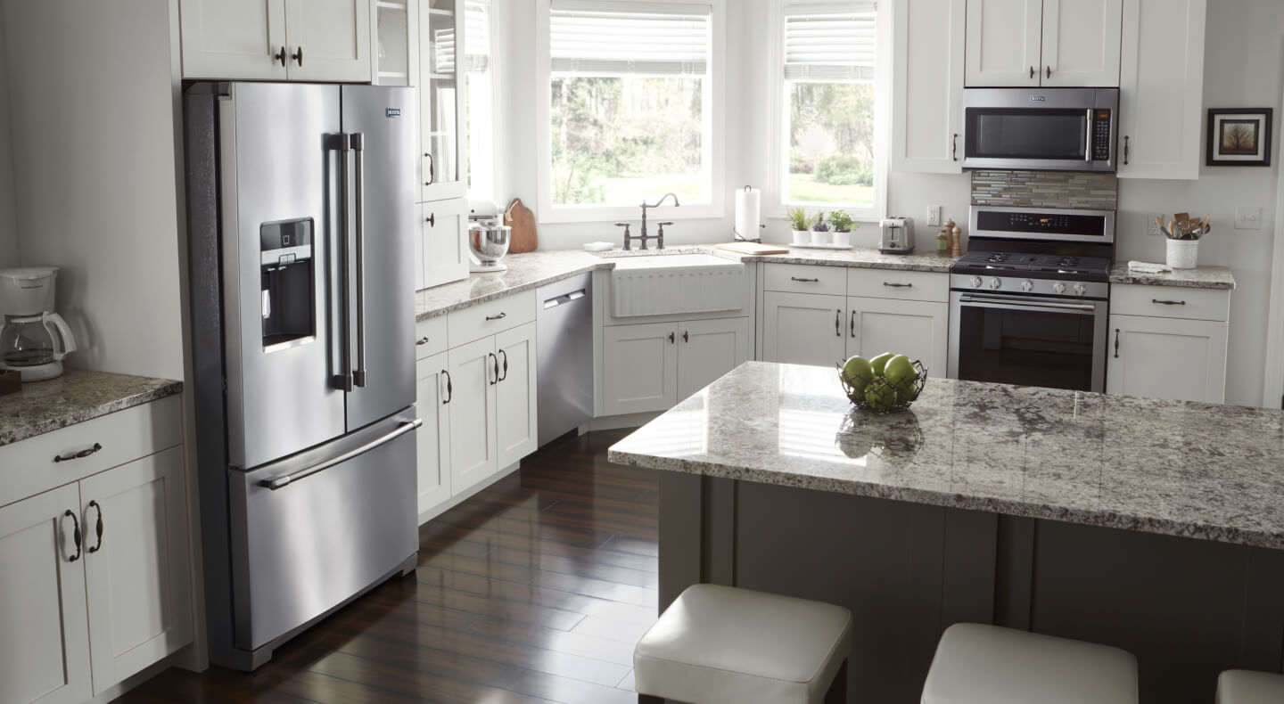 A bright, white kitchen with lots of natural light and stainless appliances, including a French door refrigerator