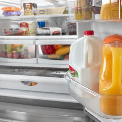 Open refrigerator door with milk and juice in gallon door bins